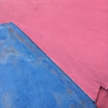 A wall featuring two painted sections, one in blue and the other in pink. The colors are applied in a rough manner, creating an abstract, textured look.