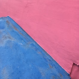 A wall featuring two painted sections, one in blue and the other in pink. The colors are applied in a rough manner, creating an abstract, textured look.