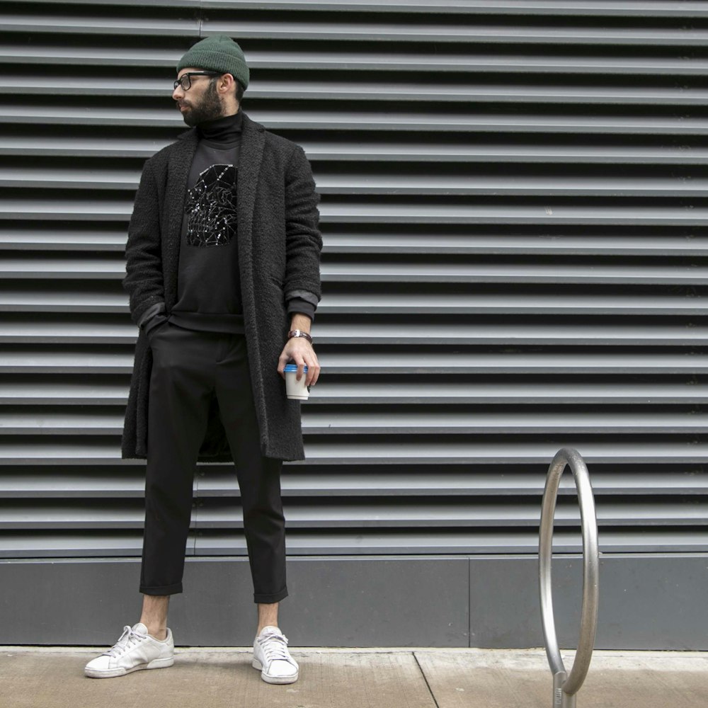 man standing while holding white plastic cup beside wall