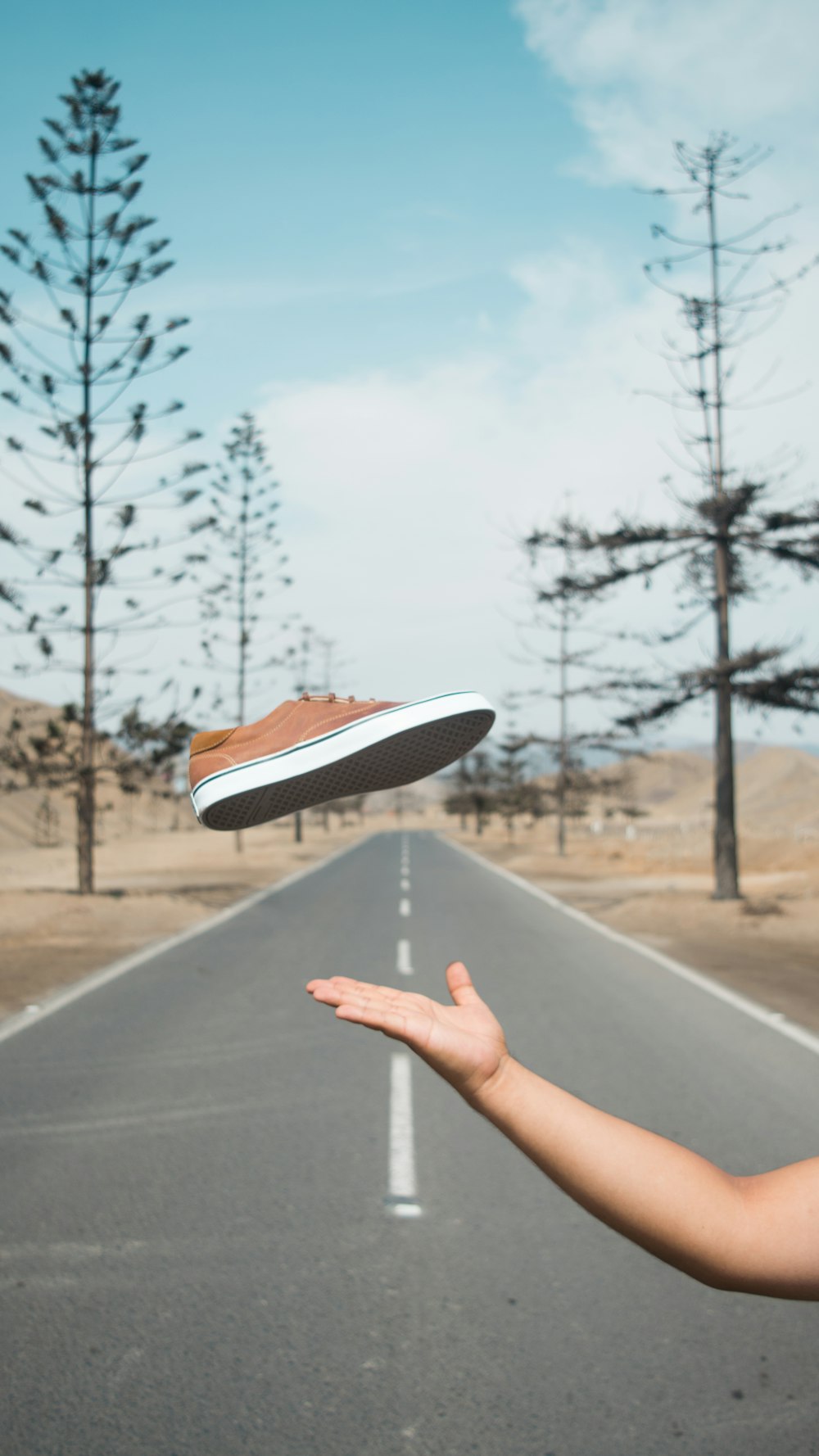 person trowing brown low-top sneaker near empty road during daytime