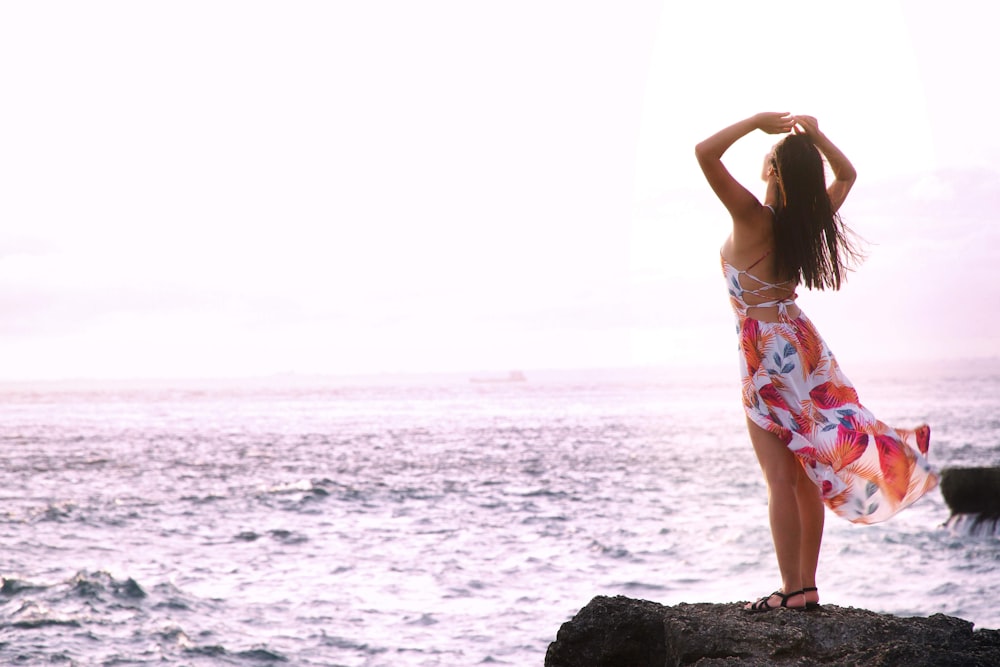 woman standing on black rock formation facing on seashore during daytime