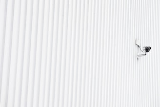 A security camera mounted on a white wall overlooking a modern office entrance.