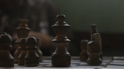 Close-up of chess pieces arranged strategically on a polished wooden chessboard under warm lighting.