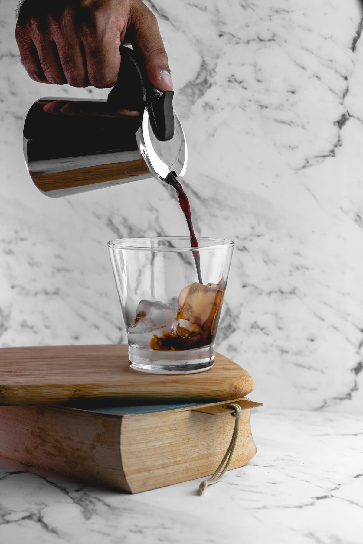 Person carefully pouring cold brew coffee concentrate into a glass cup filled with ice