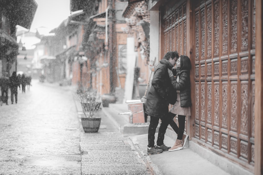 man and woman standing beside building going to kiss during daytime