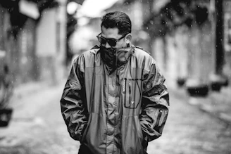 Editorial style photo of a man in a sleek coat walking through a rainy city street with reflections on the pavement
