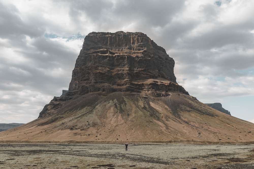 silhouette photography of person standing beside rock formation during daytime