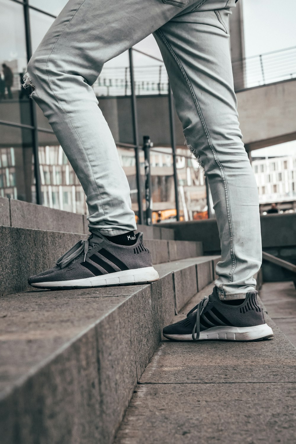 man in grey denim jeans and pair of grey and black Adidas sneakers in stairrs