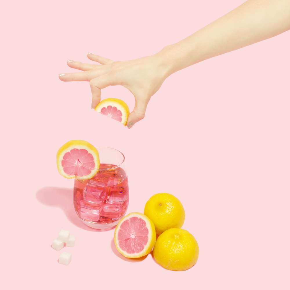 person holding slice of orange over full rock glass