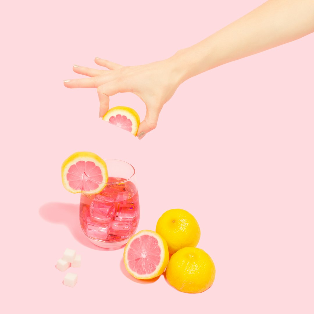 person holding slice of orange over full rock glass