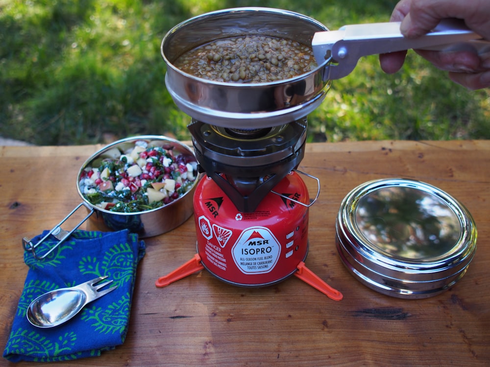 person holding pot on red single burner top on brown wooden table