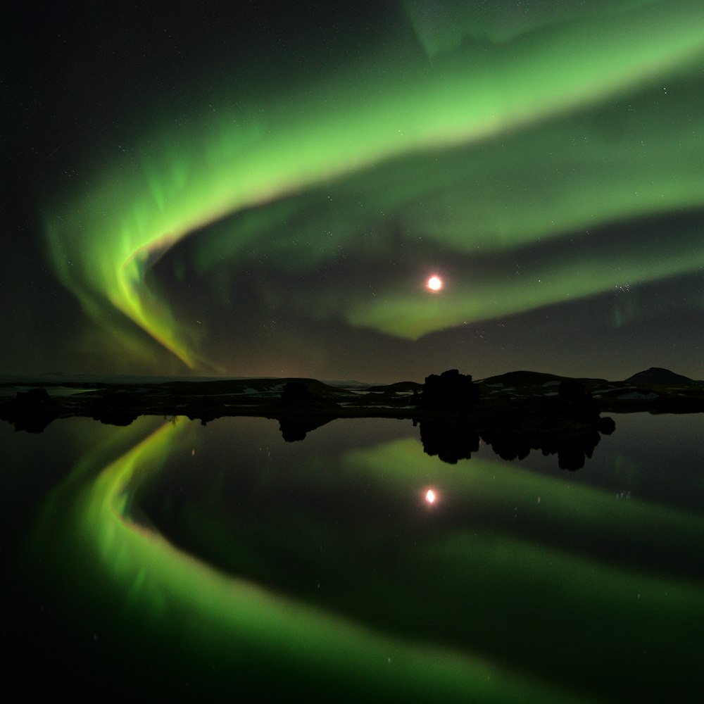 silhouette di montagna tra specchio d'acqua e aurora boreale