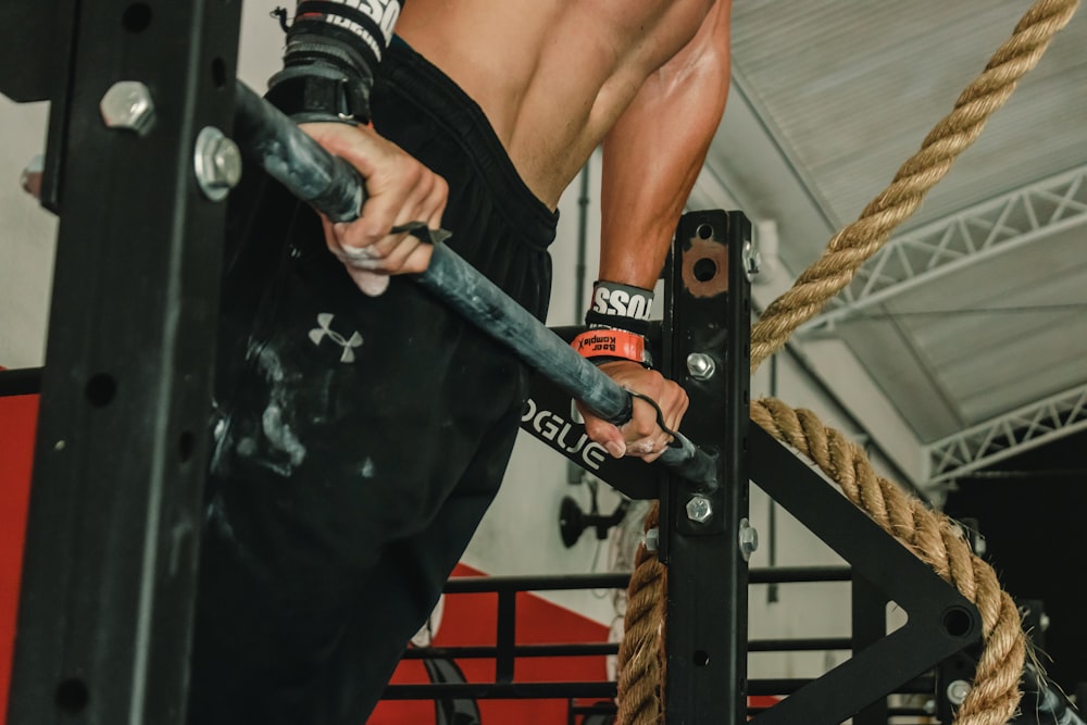 man in black pants lifting body from metal rod