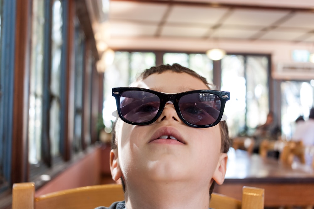 Junge mit Sonnenbrille sitzt auf braunem Stuhl