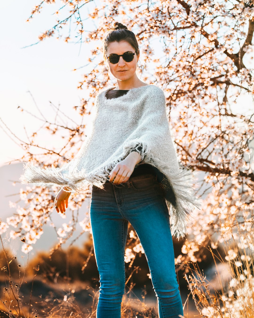 woman in grey poncho standing near cherry blossom tree