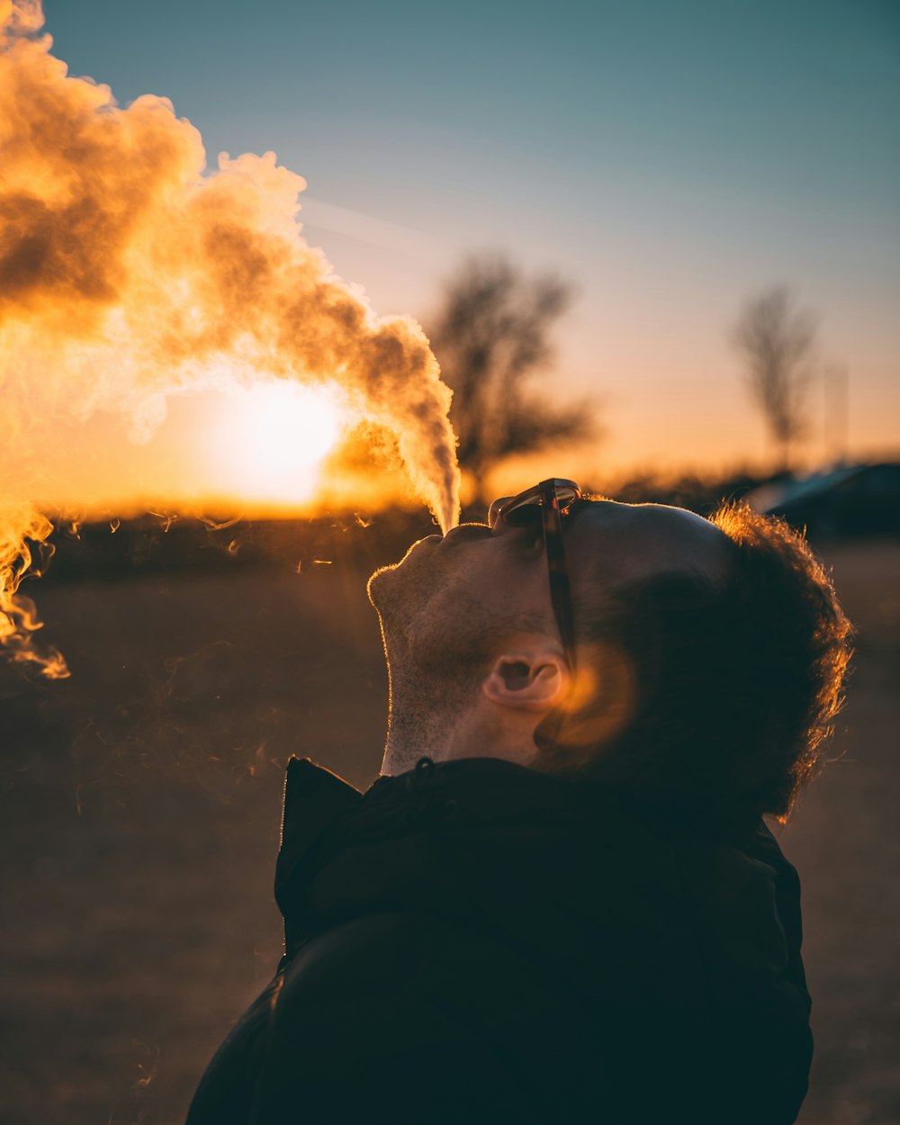 man spewing out smoke at sunset