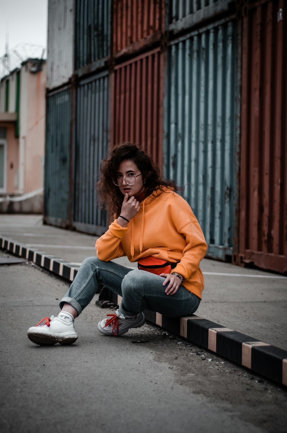 woman in orange hoodie sitting near freight container