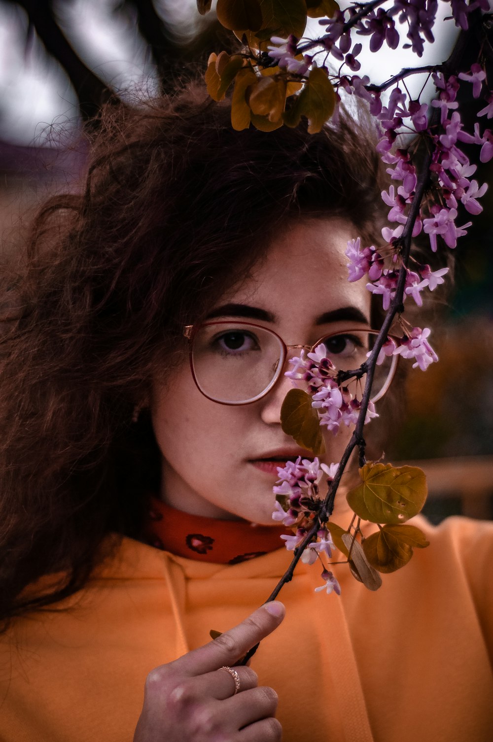 woman in orange collared shirt near purple-petaled flower