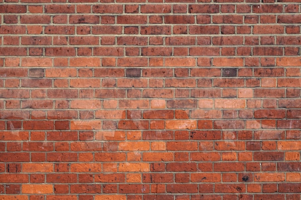 A neatly arranged pattern of red and orange brickwork forms a solid wall. The bricks are uniform in size and are laid in an even, horizontal arrangement with visible mortar lines.