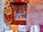 Intricate and colorful woven rugs and textiles are displayed, featuring geometric patterns in a variety of colors. They are arranged against an ornately carved wooden window or partition, behind which various decorative items, including vases and lamps, can be seen.