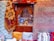 Intricate and colorful woven rugs and textiles are displayed, featuring geometric patterns in a variety of colors. They are arranged against an ornately carved wooden window or partition, behind which various decorative items, including vases and lamps, can be seen.