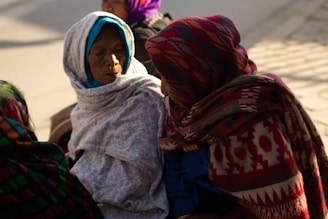 Volunteers handing out blankets to elderly women wrapped in colorful shawls.