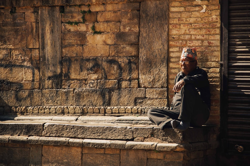 man in black jacket sitting on grey concrete ledge