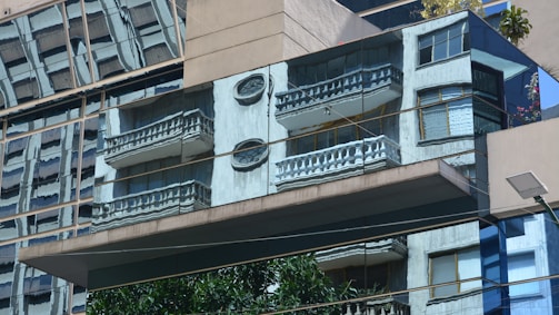 Reflections of buildings with balconies and decorative elements captured on the mirrored facade of a modern structure. The scene features distorted images of windows, balconies, and architectural details.