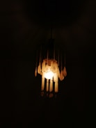 A hanging light fixture illuminates a dark space with a warm, soft glow. The fixture has decorative elements, including several hanging pieces that create a vintage or antique appearance.