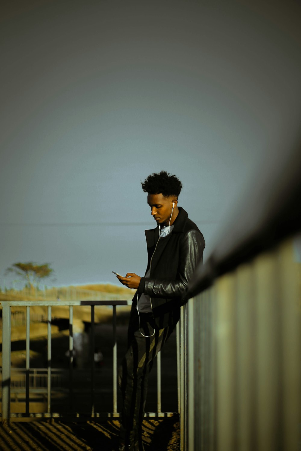 man leaning on railing using smartphone during daytime