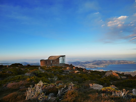 brown concrete house near rocky hill under blue and white skies in Mount Wellington Australia