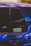 A close-up of a car window featuring a sticker with the text 'IACRO TEAM'. The car's paint appears to have an iridescent quality, reflecting various shades under the light. The window shows some reflections and blurred lights in the background.