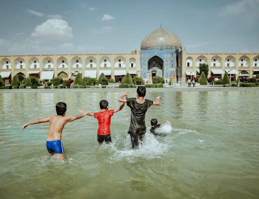 four kids on body of water beside concrete building during daytime