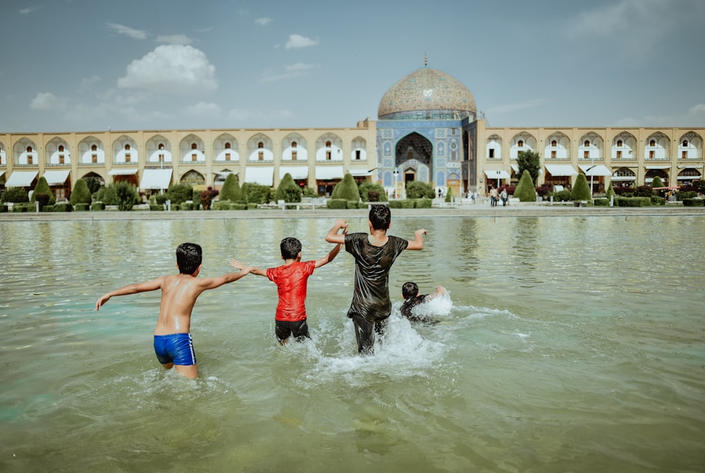 four kids on body of water beside concrete building during daytime