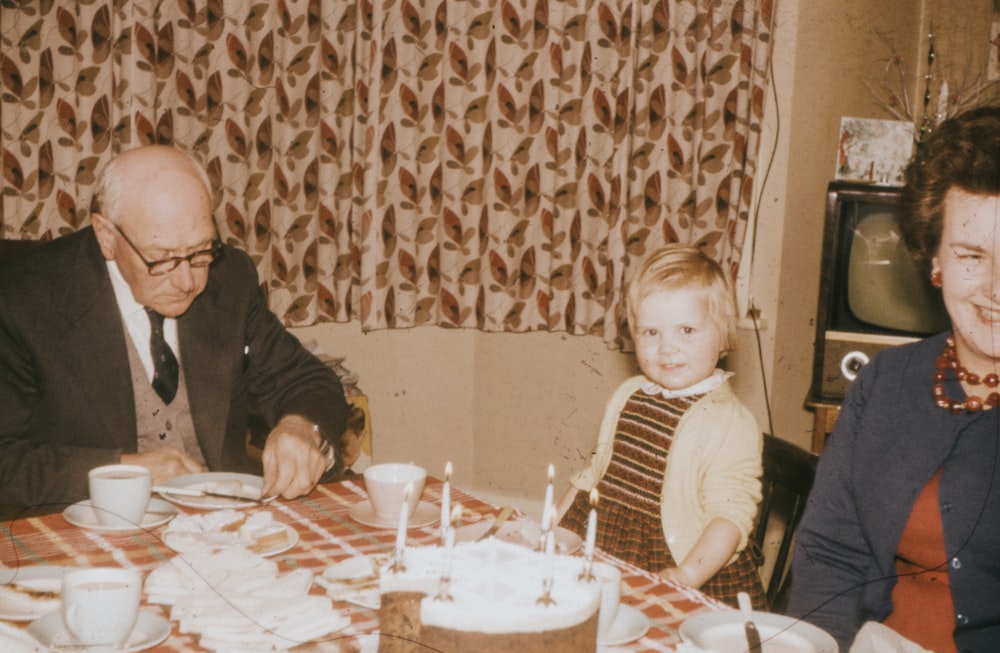 a man and two children sitting at a table with a cake
