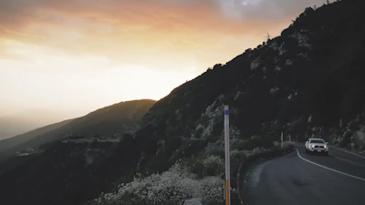 A winding mountain road with a Vibeway camper driving towards a glowing sunset.