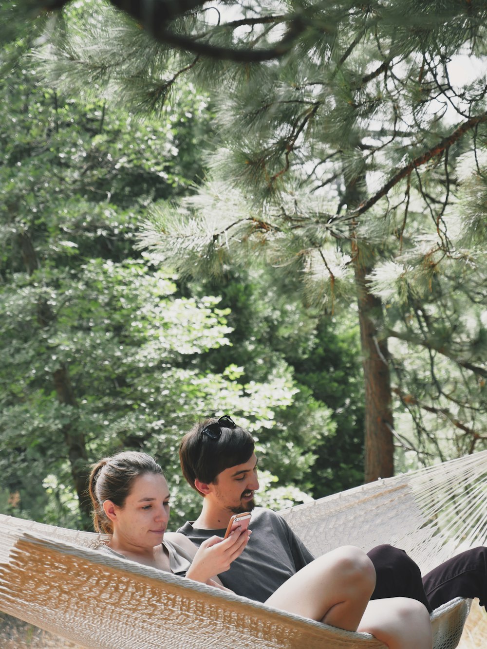 man and woman on brown hammock across green trees