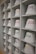 A neatly arranged display of white bucket hats sits on multiple shelves. Each hat is embroidered with words in different languages and colors, such as red, yellow, purple, and green. The hats are organized in a spacious, grid-like pattern within an indoor setting.