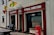 A storefront with signs for McClafferty's Bar & Lounge and Funeral Directors. The building is painted in beige with red accents. Decorative flags are displayed, and a red HB ice cream container is situated outside. A wooden bench is also visible near the entrance.
