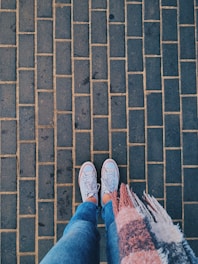 A casual lifestyle shot showing a pair of unisex rubber sneakers worn with jeans on a city sidewalk.