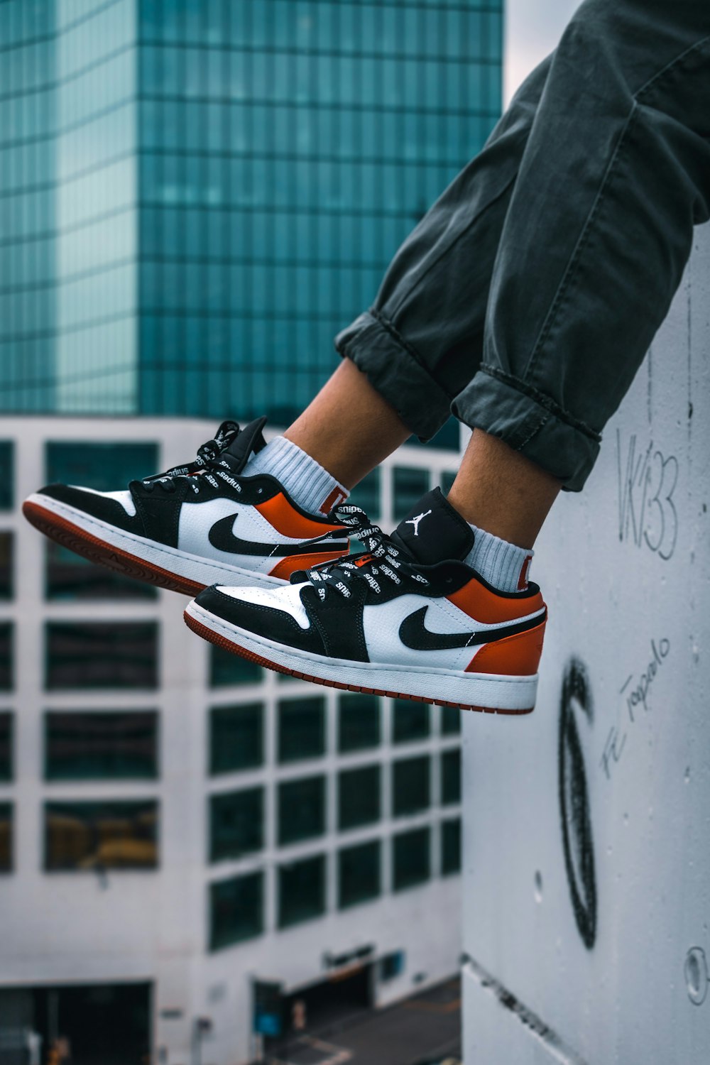 man sitting on the ledge of a building wearing Air Jordan 1 low-top shoes  photo – Free Switzerland Image on Unsplash