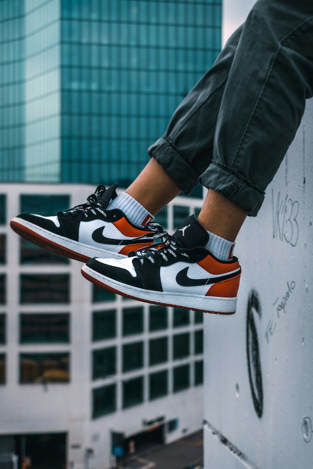 man sitting on the ledge of a building wearing Air Jordan 1 low-top shoes