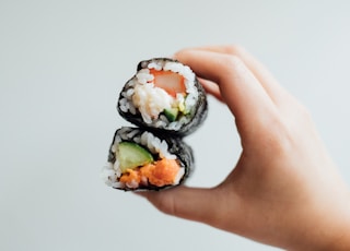 a hand holding a piece of sushi with cucumber and salmon