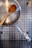 A stainless steel cooking pan with water droplets inside is placed on a metal dish rack. A wooden spoon rests inside the pan.