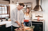 A cheerful woman chopping vegetables on a wooden board in a bright, airy kitchen with white cabinets.