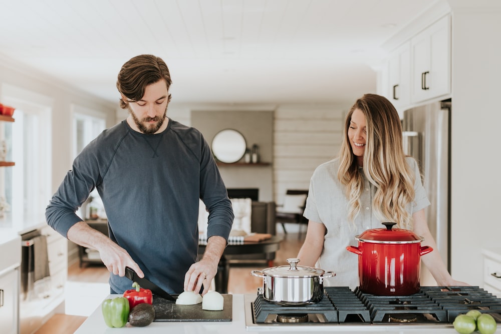 man slicing onion standing beside smiling woman