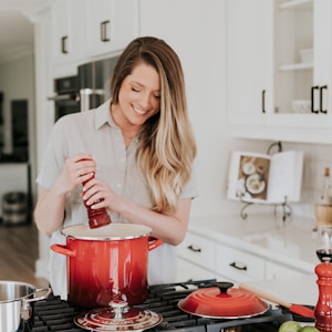 smiling woman standing and putting pepper on stock pot