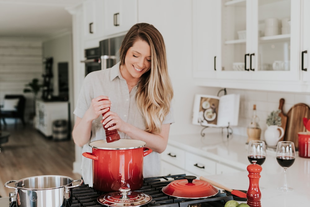 smiling woman standing and putting pepper on stock pot