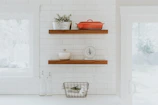 A bright kitchen corner with minimalist white shelves holding neatly arranged jars and plants.