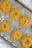 Several bundles of raw, yellow pasta nests arranged evenly on a well-used, textured baking sheet. The sheet has a light dusting of flour, and each pasta nest is neatly coiled, displaying a uniform look in size and shape.